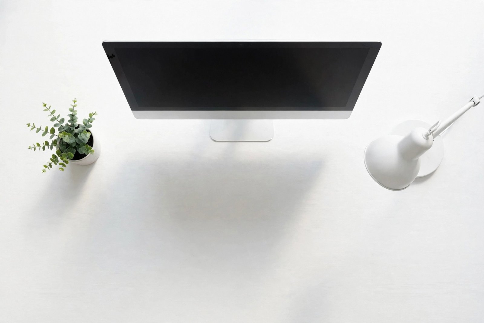  "Minimal white desk setup with monitor plant and lamp against a white wall"